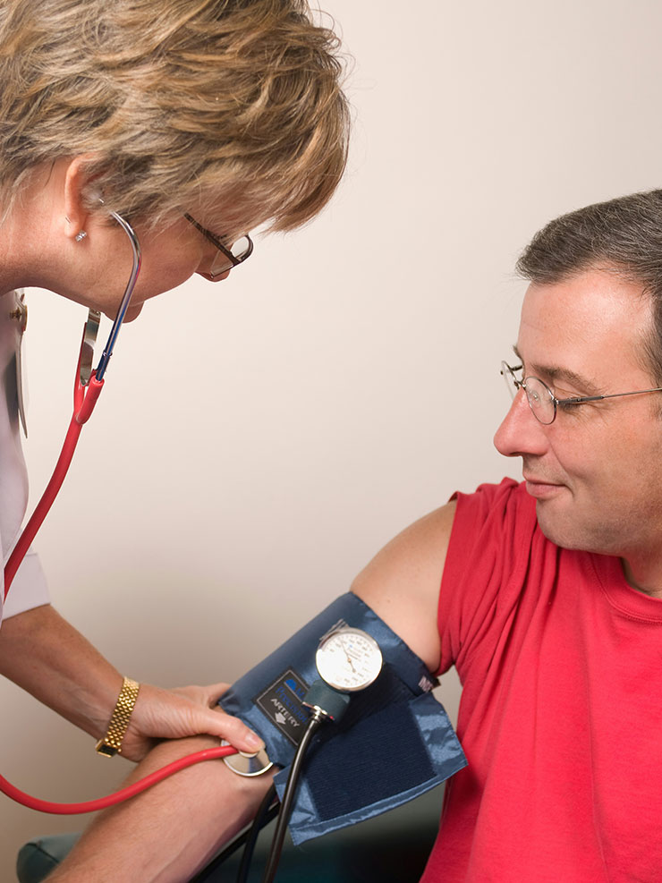 Krankenpflegerin untersucht Blutdruck eines Mannes.